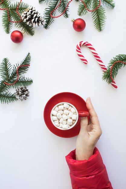 Female hand with red cup hot chocolate on the white background. Christmas composition. Top view. Copy space.