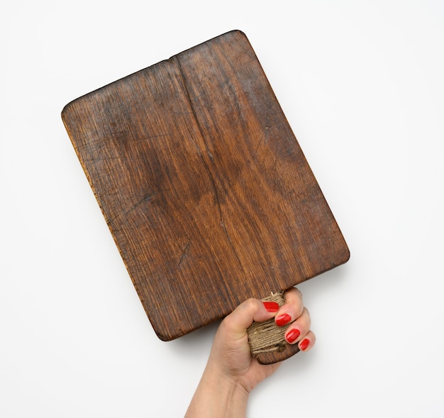 Female hand with red manicure holds blank old vintage rectangular kitchen chopping board on white background