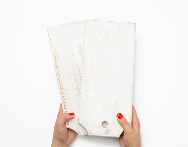 Female hand with red manicure holds empty white wooden rectangular kitchen chopping board on white background