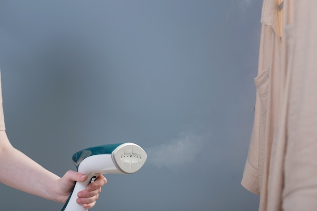 Female hand with steamer and shirt on blue background