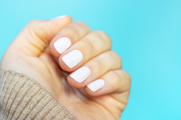 Female hand with white manicure on blue background close-up.