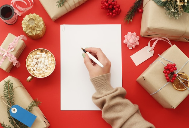 Female hand writes on a white sheet of paper among Christmas gifts