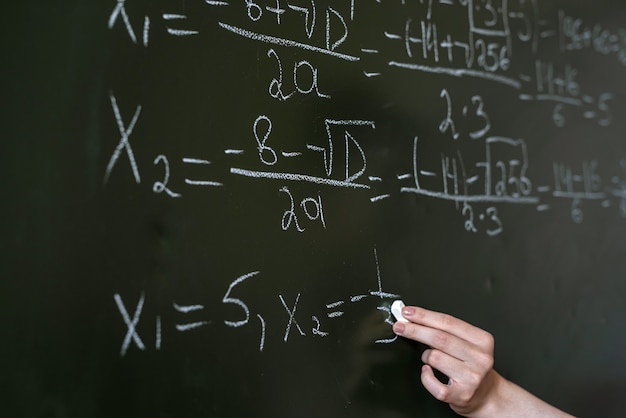 Female hand writing math formulas on the classboard, close-up