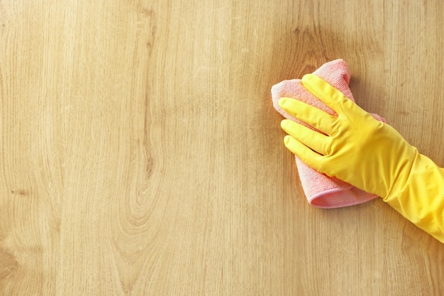 A female hand yellow rubber glove wipes a stain of dirt on the wooden parquet floor pink cloth