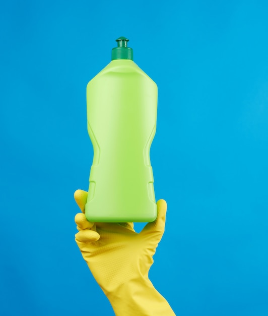 Female hand in yellow rubber gloves holds a green plastic bottle with detergent