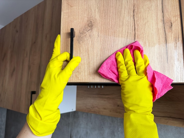 female hand in yellow rubber gloves using a rag cleaning the wooden top kitchen