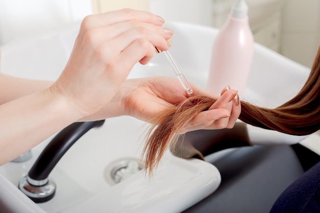 Female hands applying oil on long womans brown hair