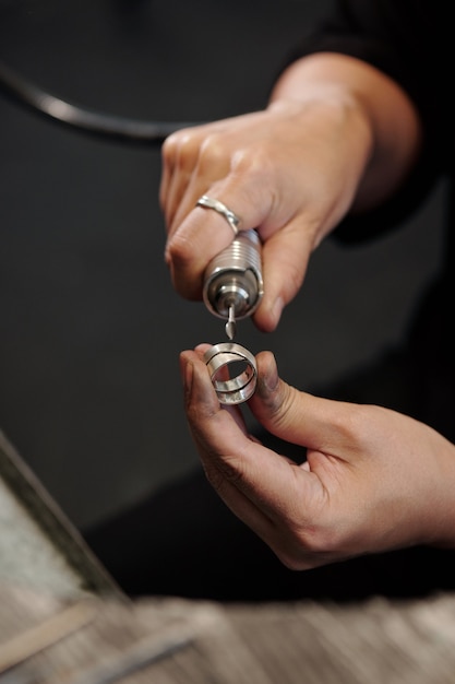 Female hands of bench jeweler forming silver ring using polisher in workshop