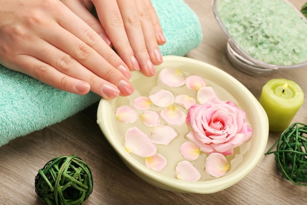 Female hands and bowl of spa water with flowers closeup