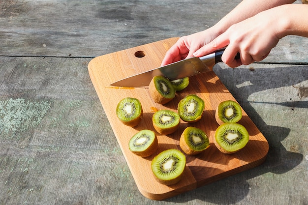 Female hands cut kiwi on a cutting board on gray vintage background