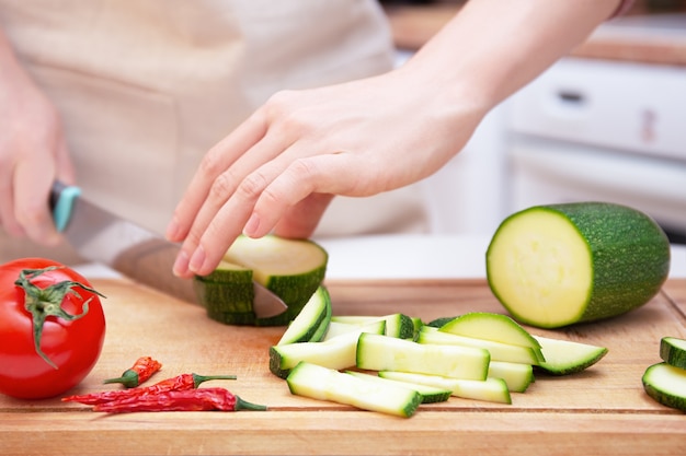 Female hands cut with a knife a young seasonal zucchini into strips on a wooden cutting board. The method of preparation of vegetables. Seasonal products, harvest. Healthy nutrition, diet.