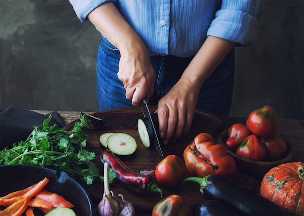 Female hands cutting eggplant on wooden board for vegan food.