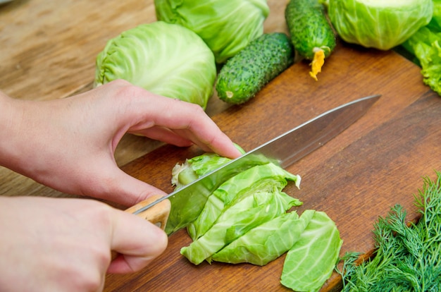 Female hands cutting fresh cabbage on a wooden cutting board