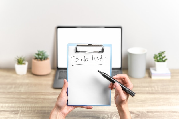 Female hands hold clipboard. Workspace with laptop on background.