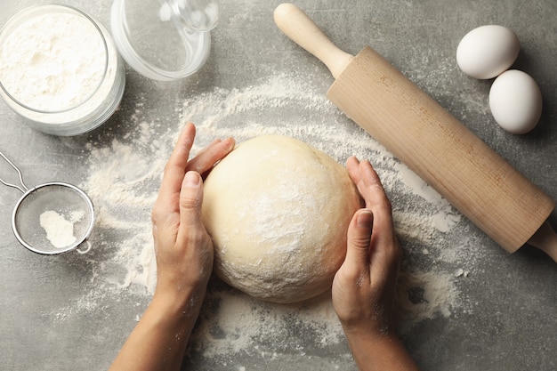 Female hands hold dough on gray surface with ingredients for baking