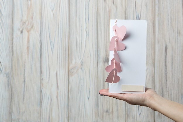 female hands hold greeting card for Valentine's Day decorated with pink hearts.