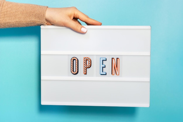 Female hands hold lightbox with the inscription open on blue background