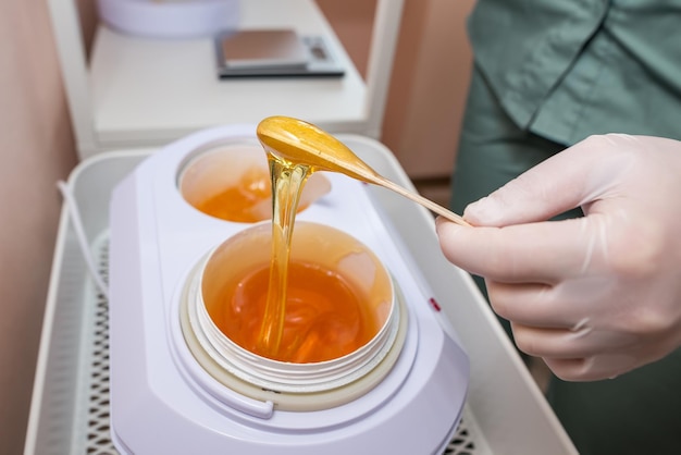 Female hands hold liquid sugar paste for hair removal on a wooden spatula The concept of body care beauty treatments