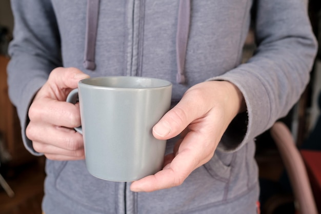 Female hands hold a mug of hot drink in the early morning in the apartment