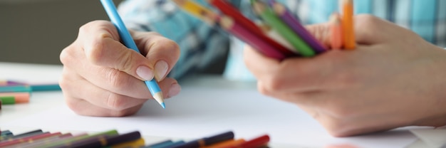 Female hands hold multicolored pencils and sheet of paper lies on table