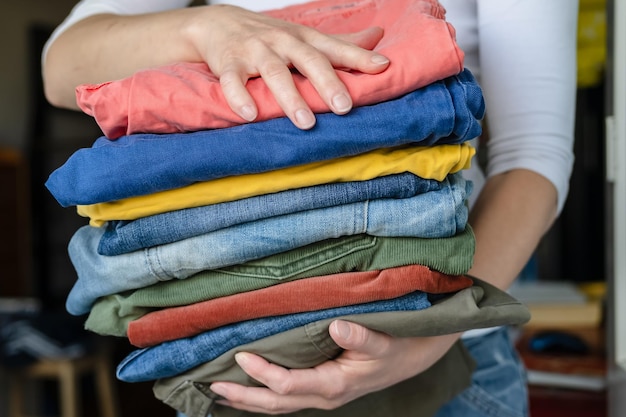 Female hands hold neatly folded trousers and jeans in bright colors after washing