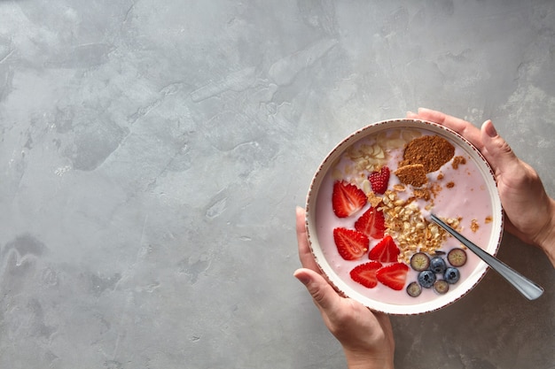 Female hands hold a plate of fresh yoghurt, berries and homemade granola