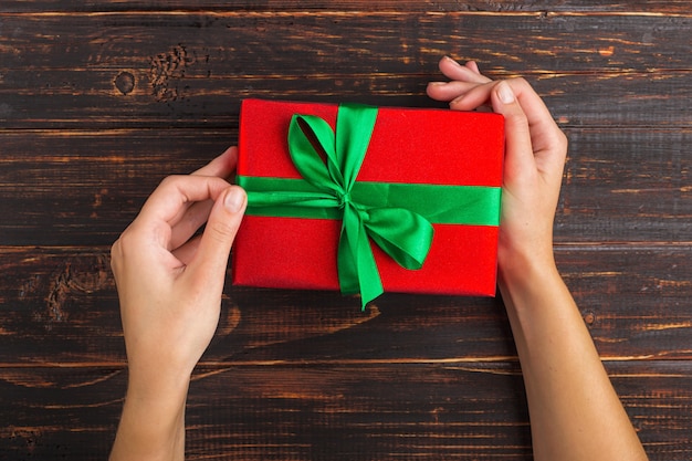 Female hands hold a red gift with a green ribbon