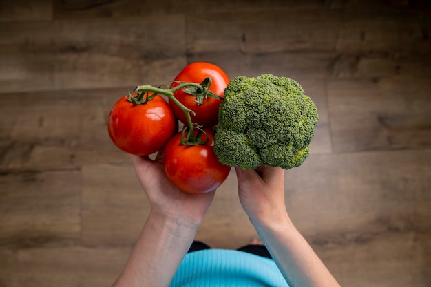 Female hands hold tomato broccoli on the background of a wooden floor Top view flat lay