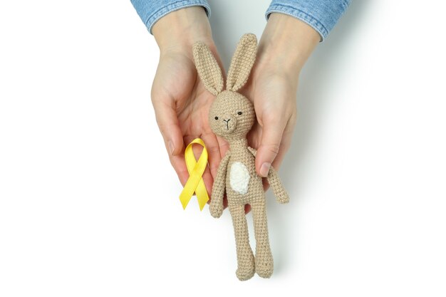 Female hands hold toy bunny and child cancer awareness ribbon, isolated on white