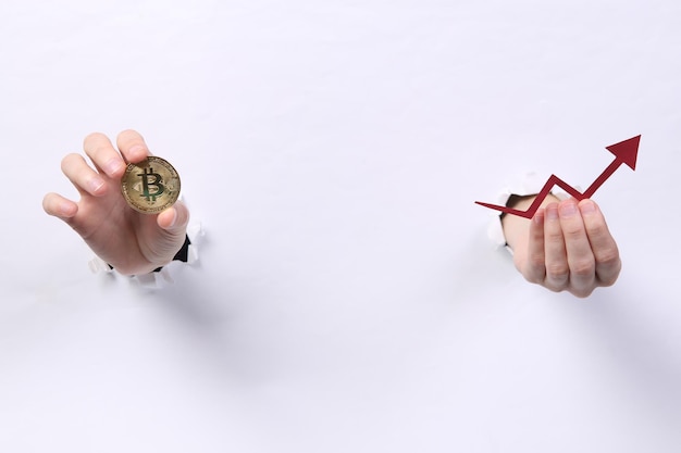 Female hands holding bitcoin and growth arrow through torn hole white paper Concept art