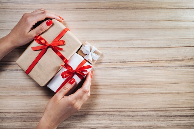 Female hands holding christmas gift boxes decorated with satin ribbons on wooden background