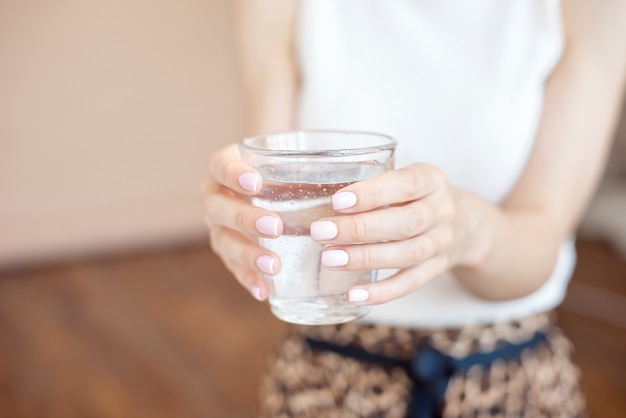 Female hands holding a clear glass of water.A glass of clean mineral water in hands, healthy drink.