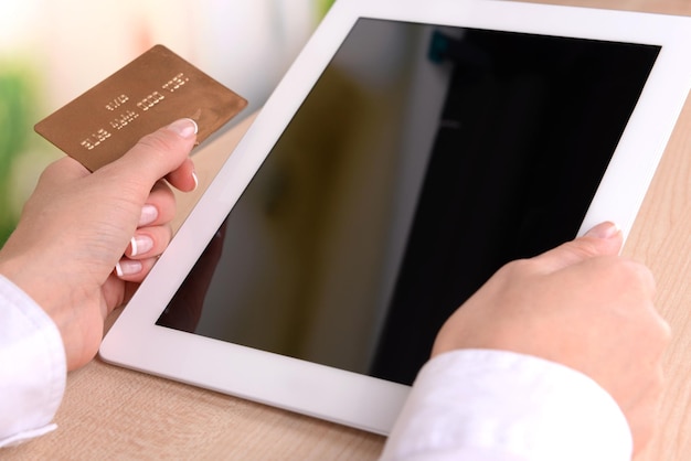 Female hands holding credit card and computer tablet on bright background