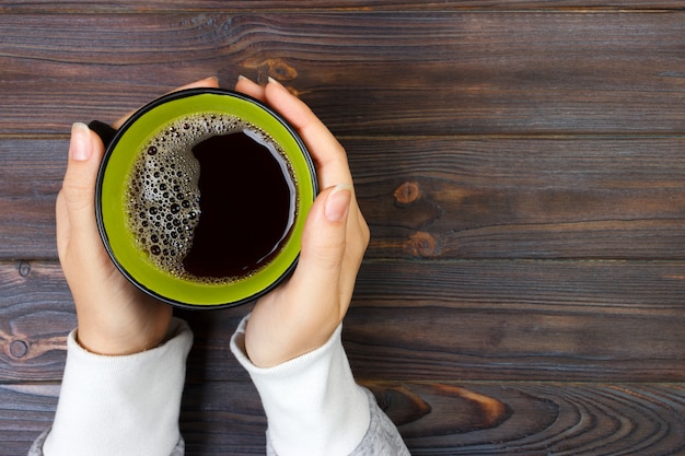 Female hands holding cup of coffee on rustic wooden table background