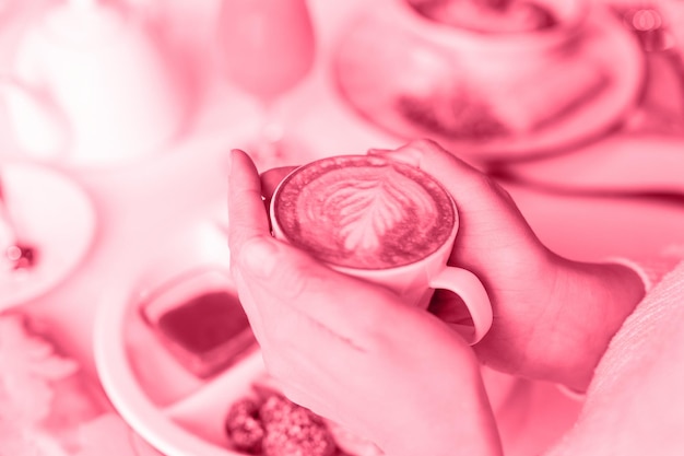 Female hands holding a cup of fresh brewed coffee with leaf latte art from foam the concept of morning breakfast and brunch toned in viva magenta trend color of the year 2023