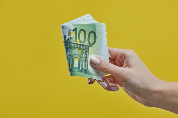 Female hands holding euro banknotes on yellow