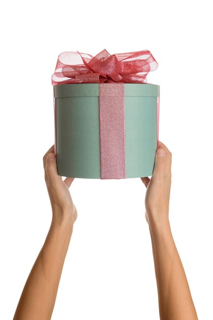 Female hands holding green round gift box with red bow on white isolated background.