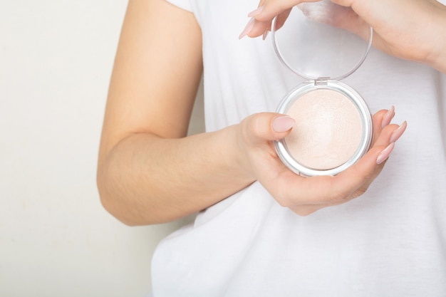 Female hands holding highlighting pressed powder with a puff 