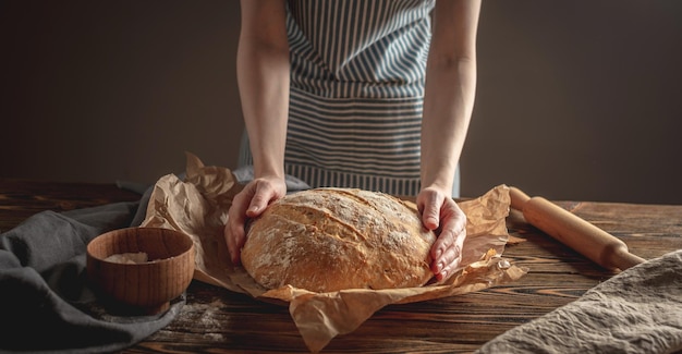 Female hands holding homemade natural bread with a Golden crust on a napkin on an old wooden background Rustic style