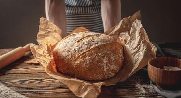 Female hands holding homemade natural bread with a Golden crust on a napkin on an old wooden background Rustic style