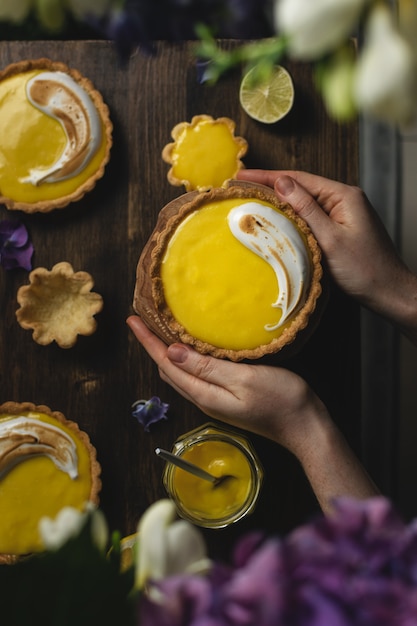 Female hands holding Lemon meringue tart on dark rustic table