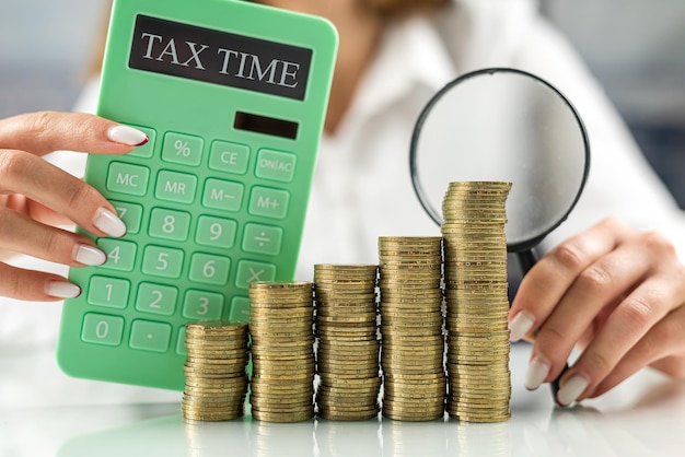 Female hands holding a magnifying glass on a mountain of coins and a calculator nearby