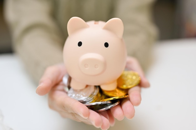 A female hands holding a piggy bank and coins over white table closeup image