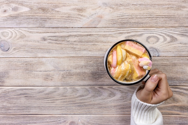 Female hands holding pink cup of coffee with coulorfull marshmallow