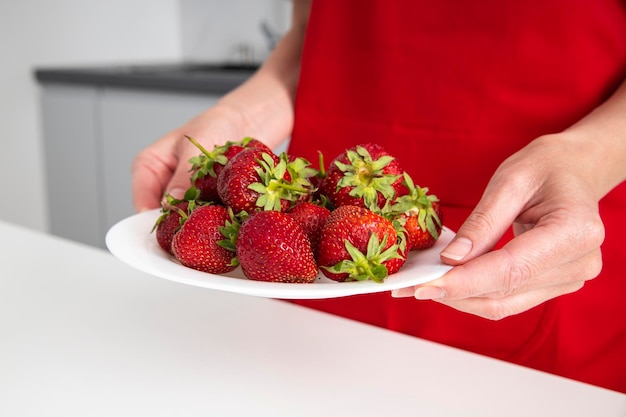 Female hands holding a plate with strawberries in the kitchen