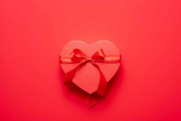 Female hands holding red heart gift box on red background. Valentine's Day composition