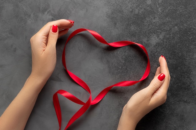 Female hands holding red ribbon heart on dark background