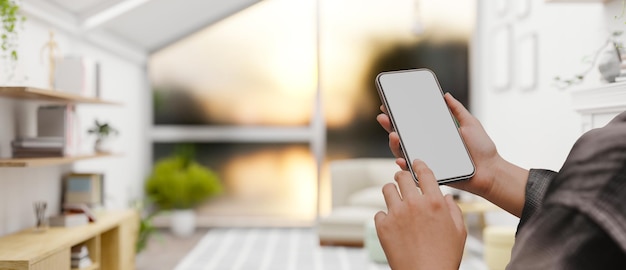 A female hands holding a smartphone over blurred minimal home living room in the background