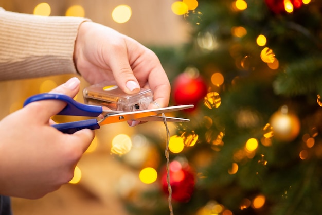 Female hands holding socket with two AA batteries and scissors trying to cut the wire of garland