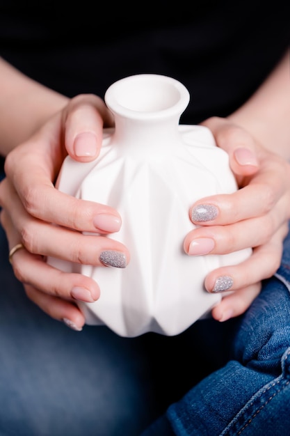 Female hands holding white ceramic vase Manicure with pink and gray color nail polish